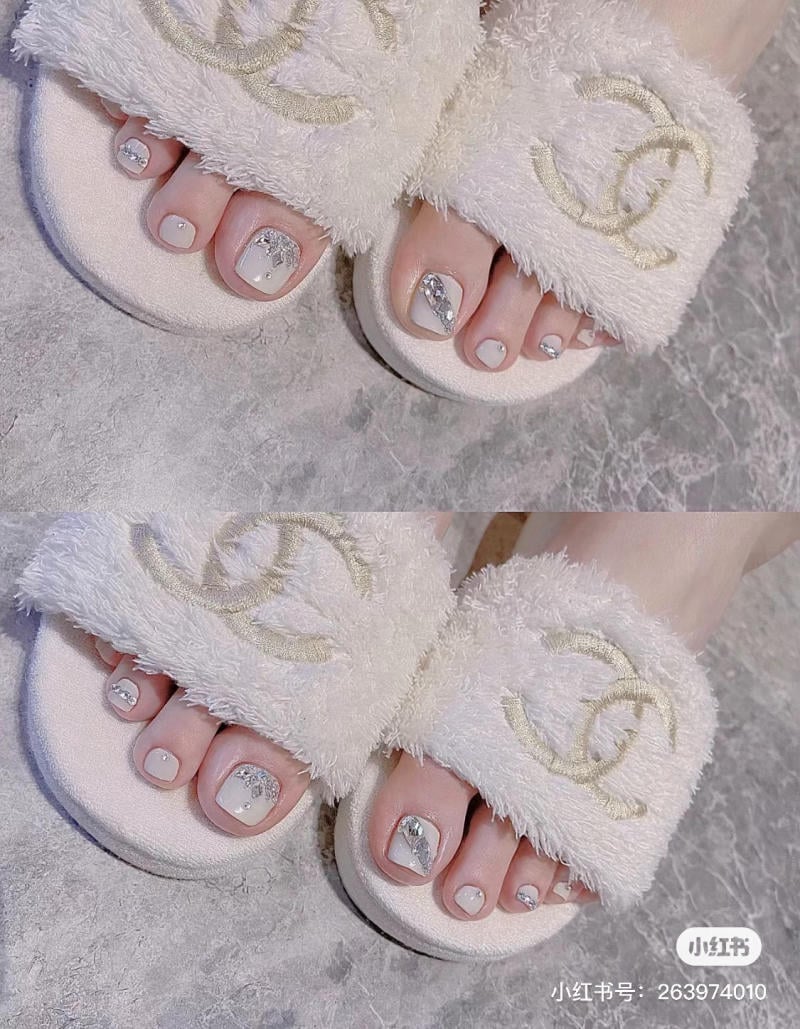 nail-chan-dinh-da__14__cba69ecfe6e24adea1e606c45ae77aea Bàn chân mang dép lông trắng, móng chân được sơn màu trắng và trang trí kim tuyến bạc.