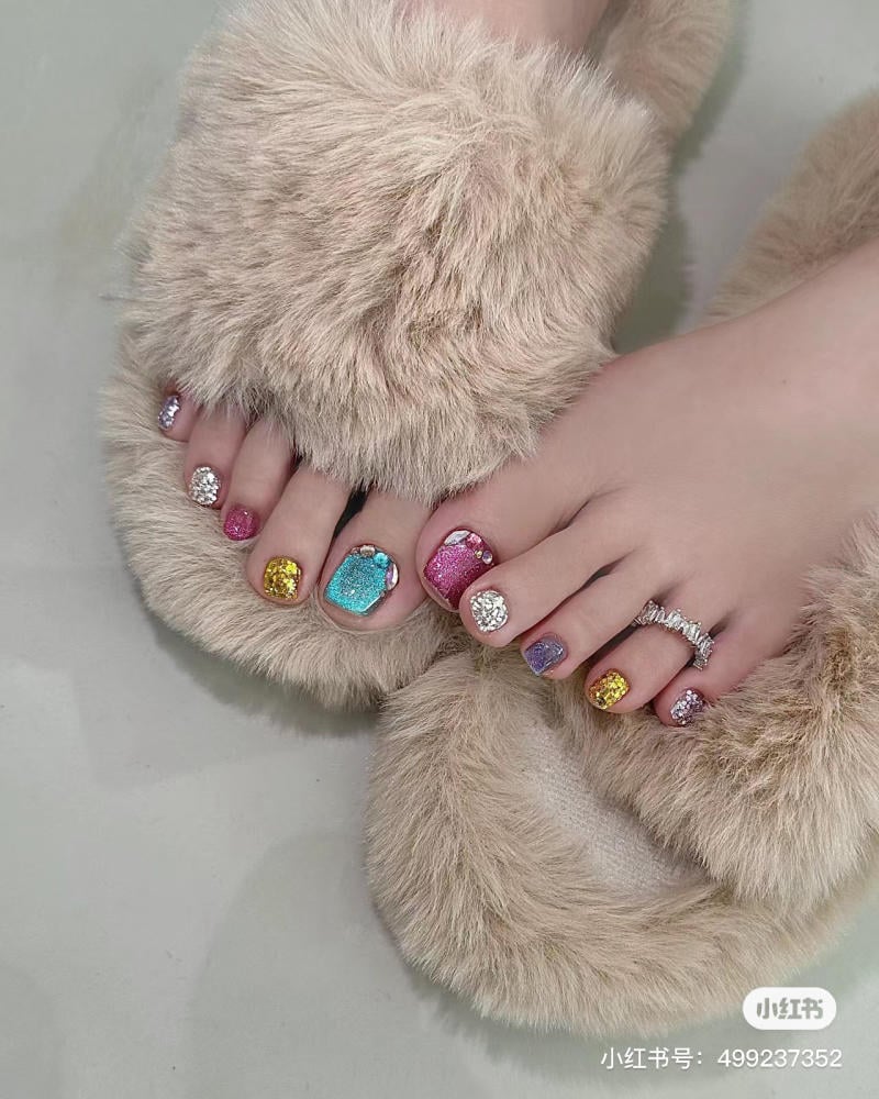nail-chan-dinh-da__18__3e3dd2e7e44c4d688eb6a28a58d28789 Bàn chân mang dép lông mềm, móng chân được sơn màu sắc rực rỡ và đính đá trang trí lấp lánh.