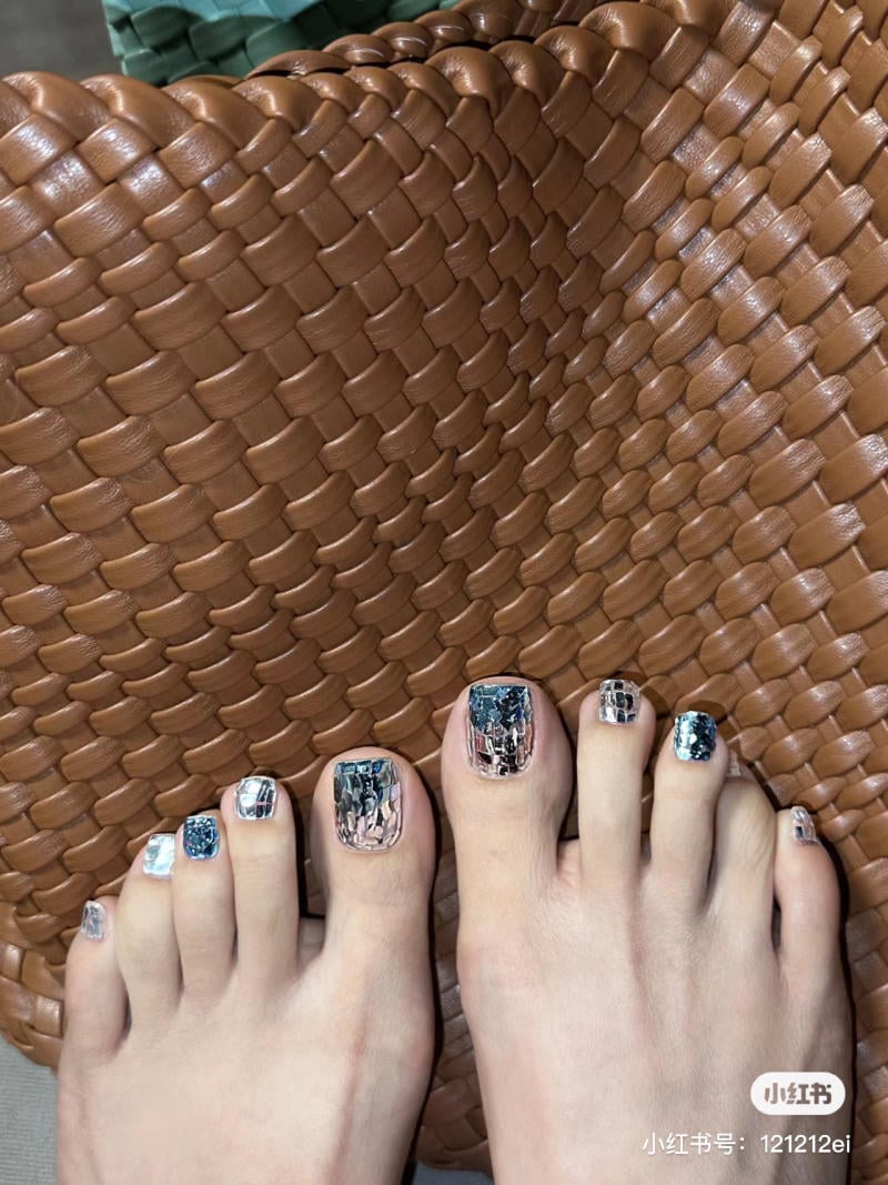 nail-chan-dinh-da__23__edb53c341b6c4529847b8e9a25699400 Bàn chân với móng chân được trang trí nghệ thuật, đặt trên bề mặt đan từ chất liệu màu nâu.