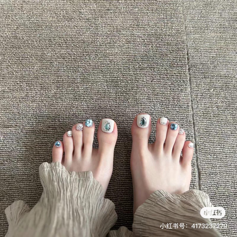 nail-chan-dinh-da__44__86225405fa2b4450bf95dce02c165602 Bàn chân với móng được trang trí họa tiết trên nền thảm xám, mặc quần ống rộng.
