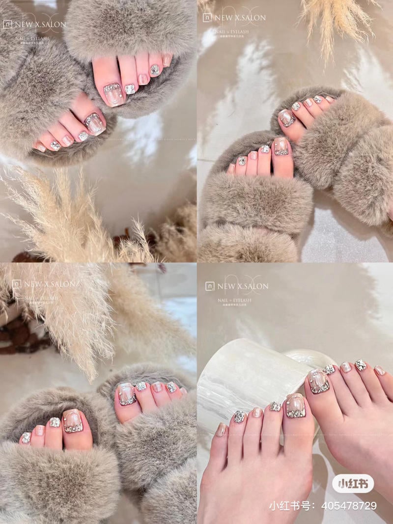 nail-chan-dinh-da__7__f29cc4964d92489991d25c52e3a5eeaf Bộ móng chân được trang trí với hoa văn lấp lánh và đi dép lông màu xám, đặt trên nền sáng.