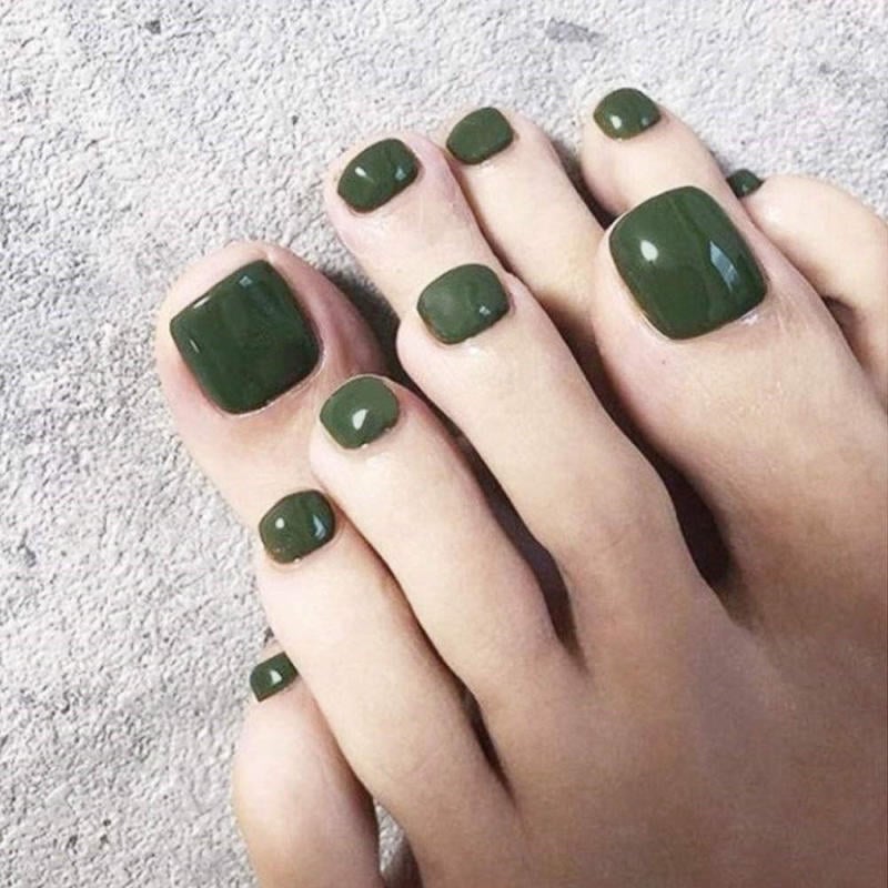 Bàn chân với móng chân được sơn màu xanh lá cây đậm, đặt trên bề mặt màu xám nhạt.