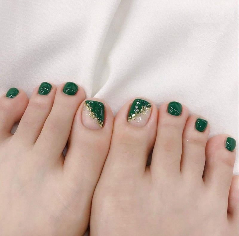 Bàn chân với móng được sơn màu xanh lá, có họa tiết ánh kim trên nền vải trắng.