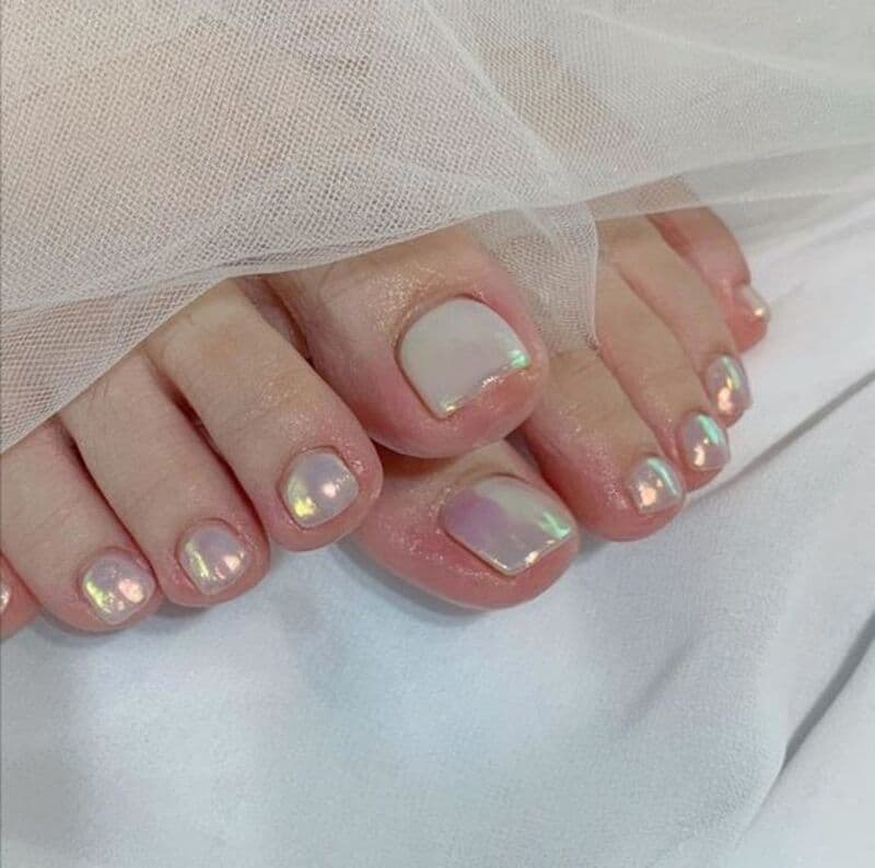 99+ mẫu nail đính đá vừa XINH vừa SANG cho nàng tự tin ra ngoài 59 Bàn chân với móng chân được sơn màu ánh kim, đặt trên vải trắng và phủ vải voan trong suốt.