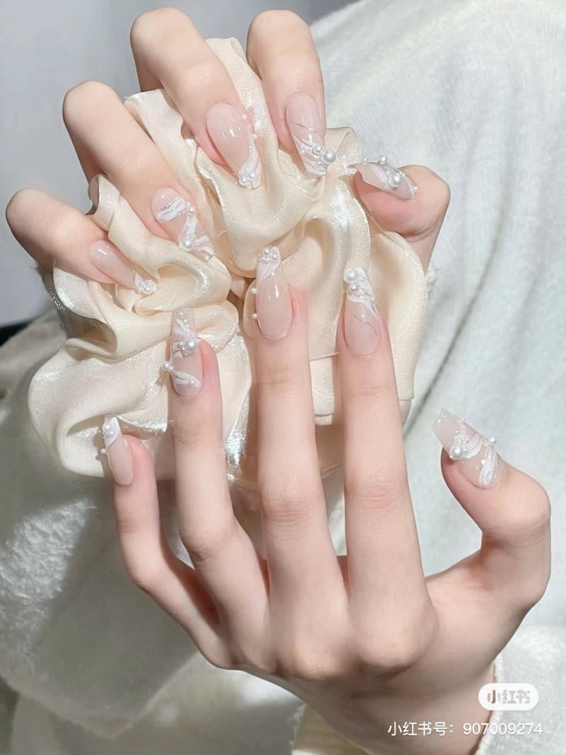 Hai bàn tay với móng tay được trang trí tinh xảo, cầm một chiếc nơ lụa màu trắng ngà.