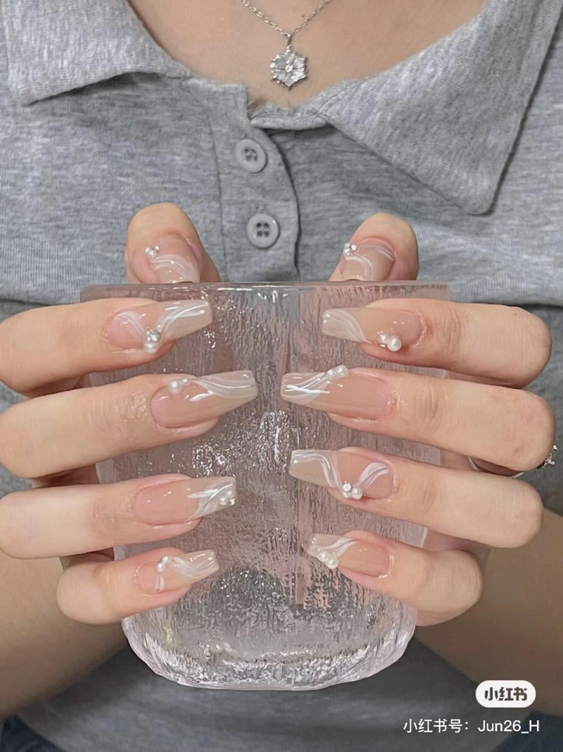 Người mặc áo xám cầm ly thủy tinh, móng tay được trang trí với họa tiết trắng và đính hạt.