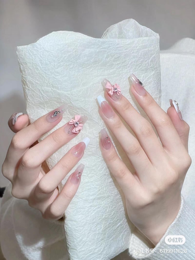 Bàn tay với móng tay dài được trang trí hoa và đá, đặt trên nền giấy trắng nhăn.