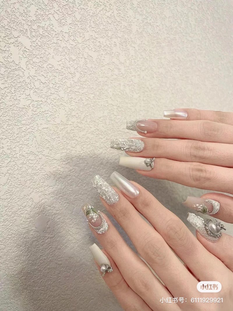 Bàn tay với móng tay dài được trang trí họa tiết lấp lánh và phụ kiện trên nền tường có kết cấu.