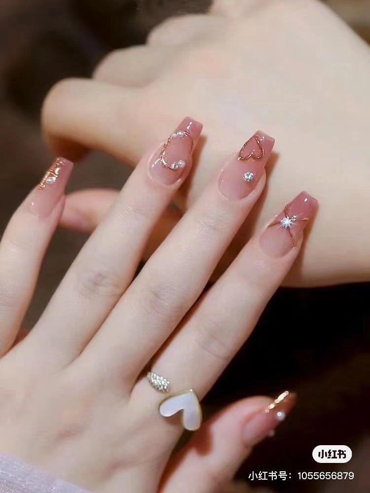 Bàn tay với móng tay được trang trí tinh xảo, đeo nhẫn hình trái tim, nền mờ.