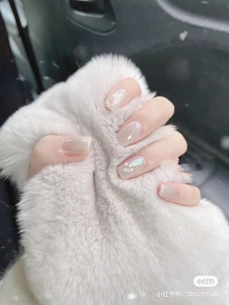 Bàn tay với móng tay sơn bóng, cầm áo lông màu trắng, nền là cửa xe ô tô.