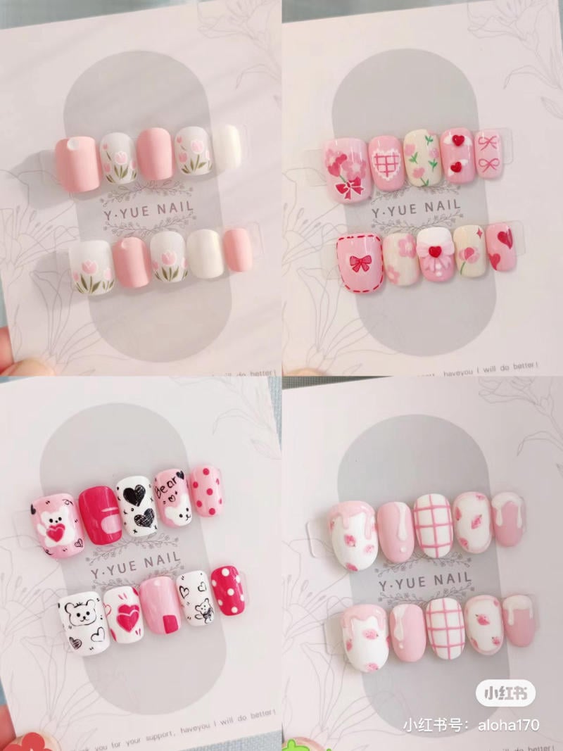 Bộ sưu tập móng tay giả với các thiết kế hoa, trái tim, và họa tiết dễ thương trên nền hồng và trắng.