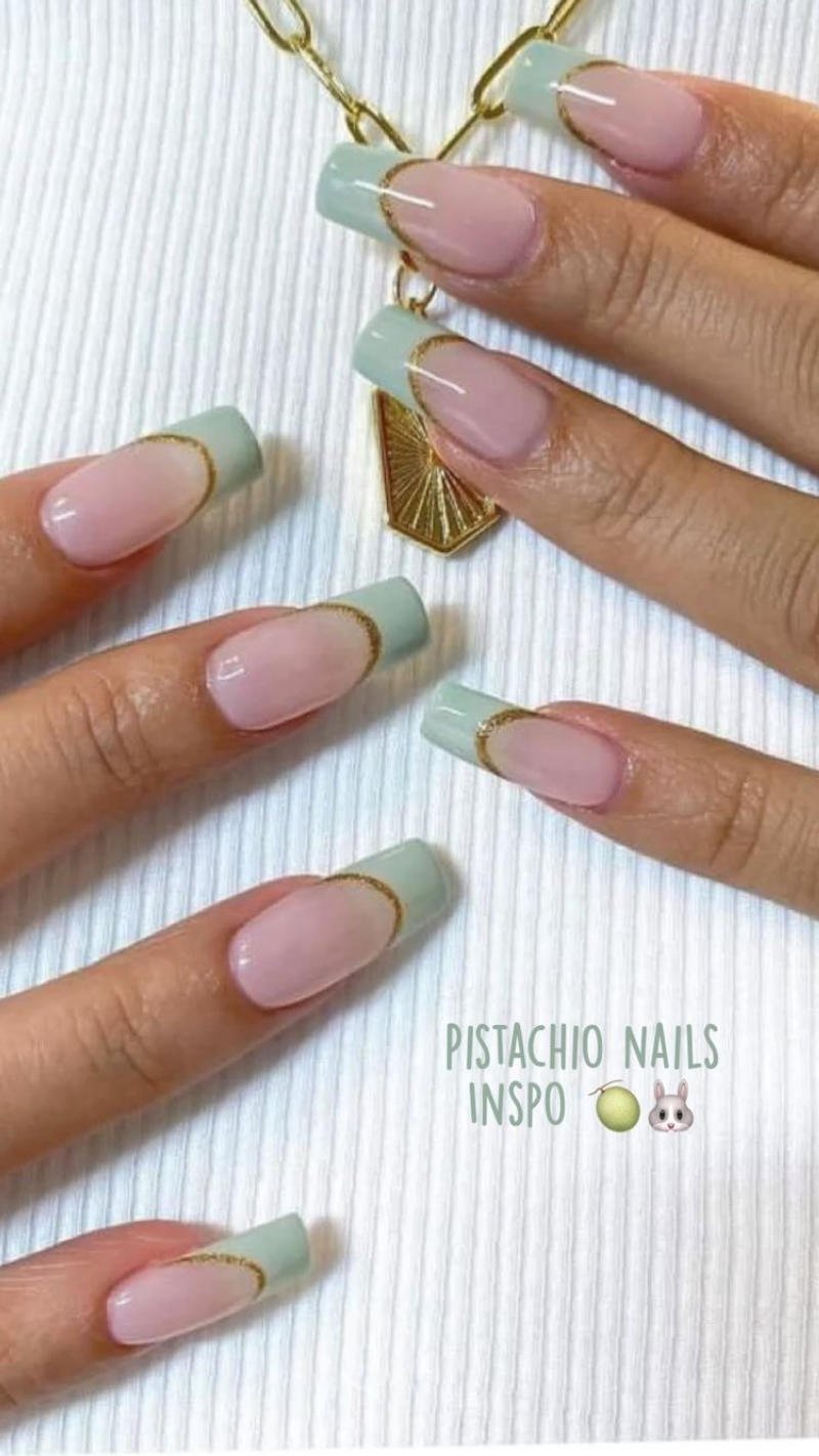 Bàn tay với móng tay dài, sơn màu xanh pastel và hồng nhạt, viền vàng, trên nền vải trắng.
