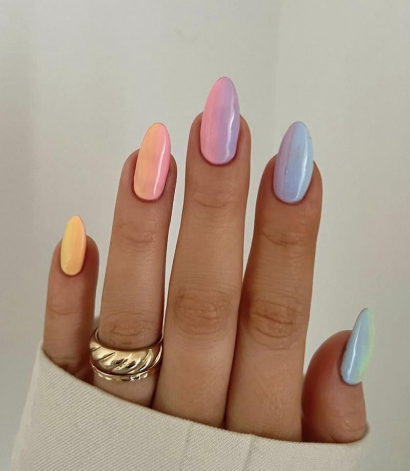 Bàn tay với móng tay sơn màu pastel ombre, mỗi ngón có màu sắc khác nhau, đeo nhẫn bạc lớn, áo màu sáng.