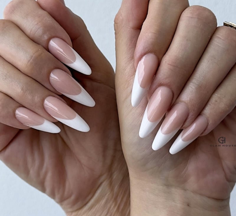 Bàn tay với móng tay dài, nhọn, sơn màu nude và đầu móng trắng, kiểu dáng thanh lịch và hiện đại.