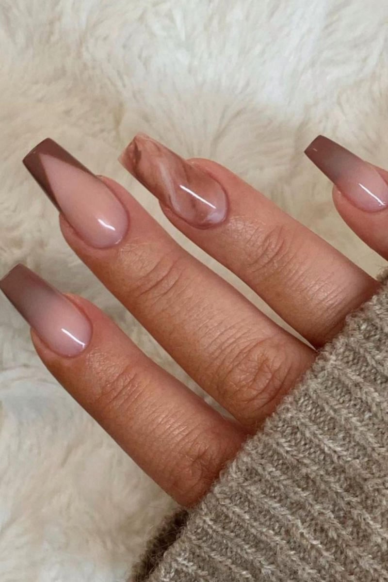 Bàn tay với móng tay dài được sơn màu nâu và hồng, họa tiết ombre và vân đá, trên nền vải màu trắng.