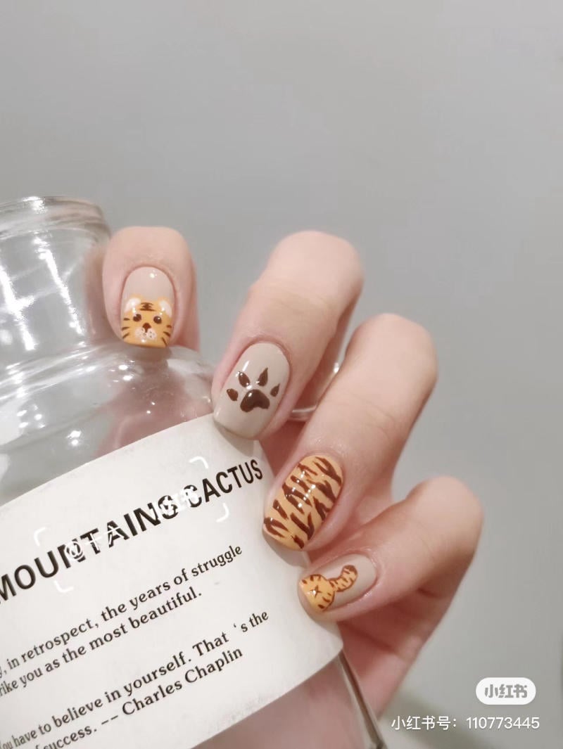 Bàn tay với móng tay trang trí họa tiết động vật, cầm một chai thủy tinh có dòng chữ in tiếng Anh.