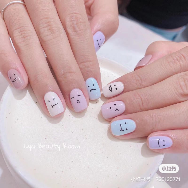 Bàn tay với móng tay được trang trí màu pastel và hình vẽ khuôn mặt cảm xúc khác nhau.