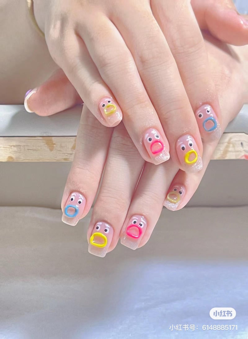 Bàn tay với móng tay sơn hình khuôn mặt hoạt hình nhiều màu sắc khác nhau trên nền trắng.