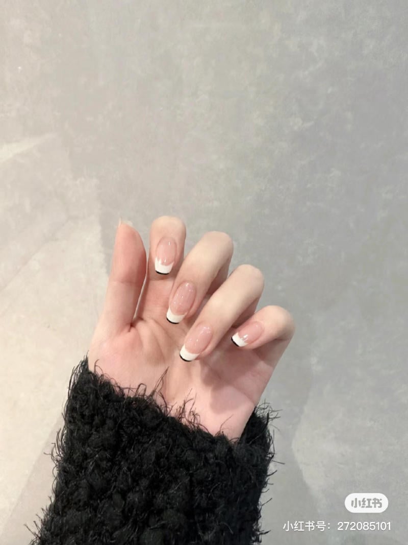Bàn tay với móng tay được sơn kiểu Pháp, áo len màu đen, nền tường xám.
