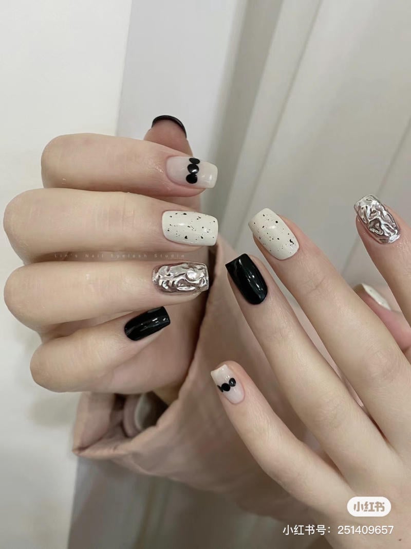 Bàn tay với móng tay được sơn màu đen, trắng và bạc, có họa tiết chấm bi và hoa văn độc đáo.