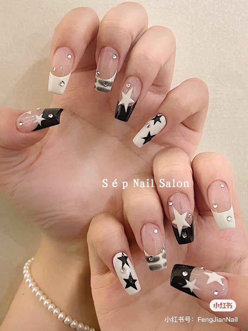 Bàn tay với móng tay sơn họa tiết ngôi sao đen trắng và đính đá lấp lánh.