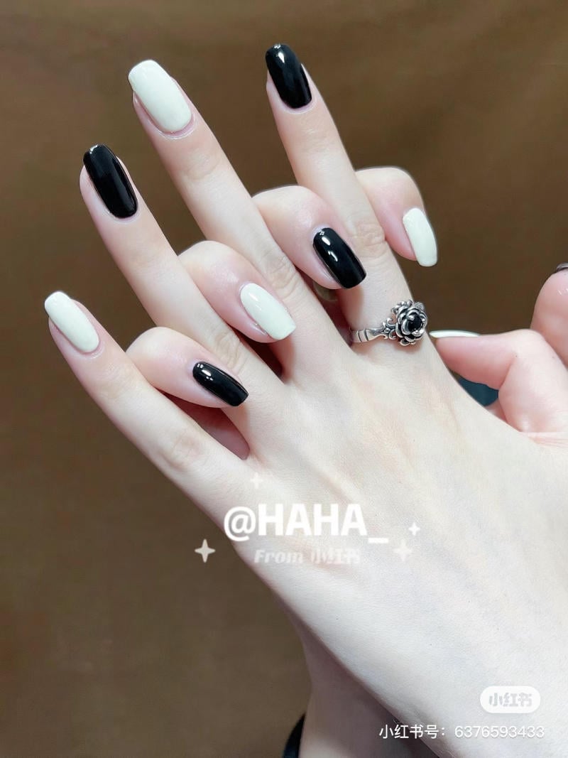Bàn tay đeo nhẫn, móng tay sơn màu đen và trắng xen kẽ, nền màu nâu.
