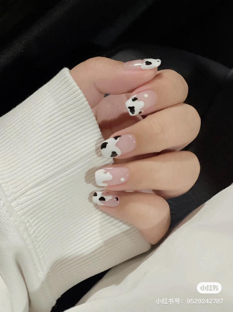 Bàn tay với móng tay được trang trí họa tiết đen trắng, giống như họa tiết da bò, trên nền móng màu hồng nhạt.