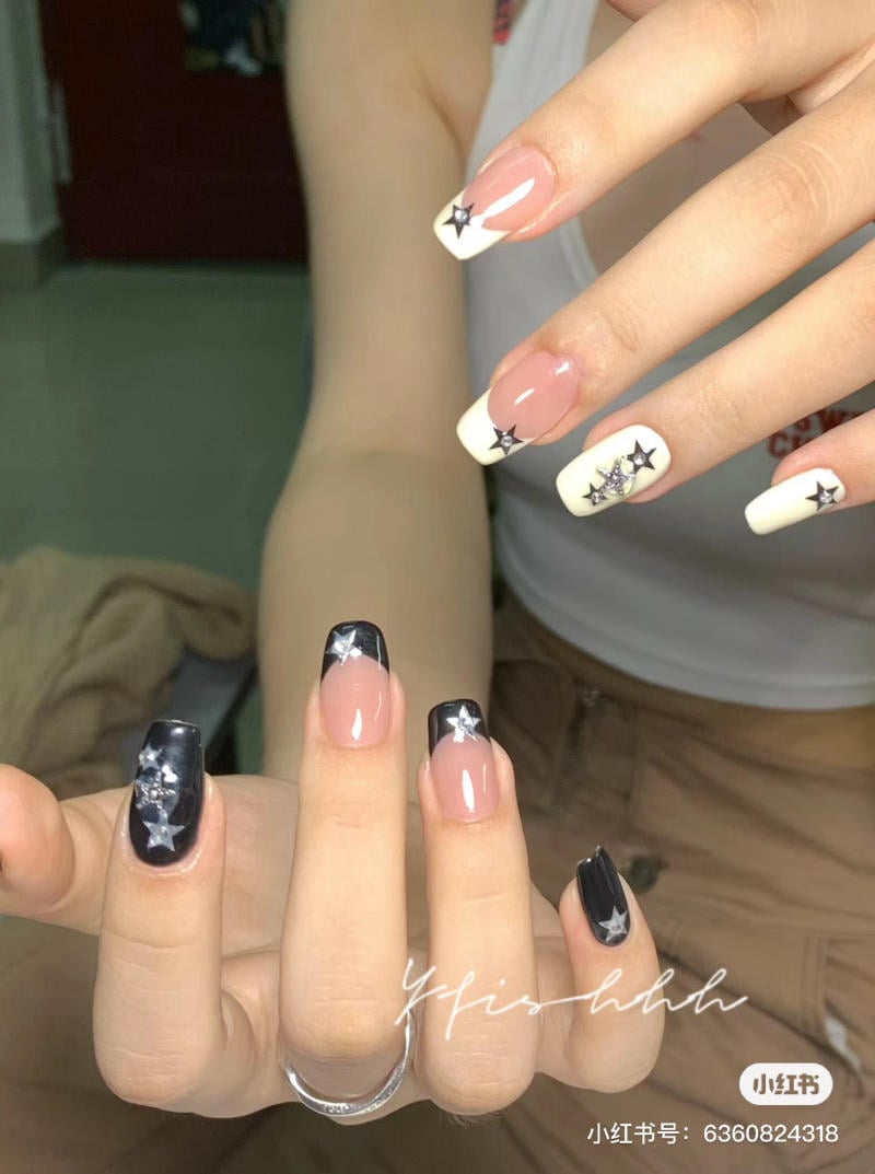 Bàn tay với móng tay được sơn màu đen và trắng, trang trí hình ngôi sao, đang giơ lên trong phòng.