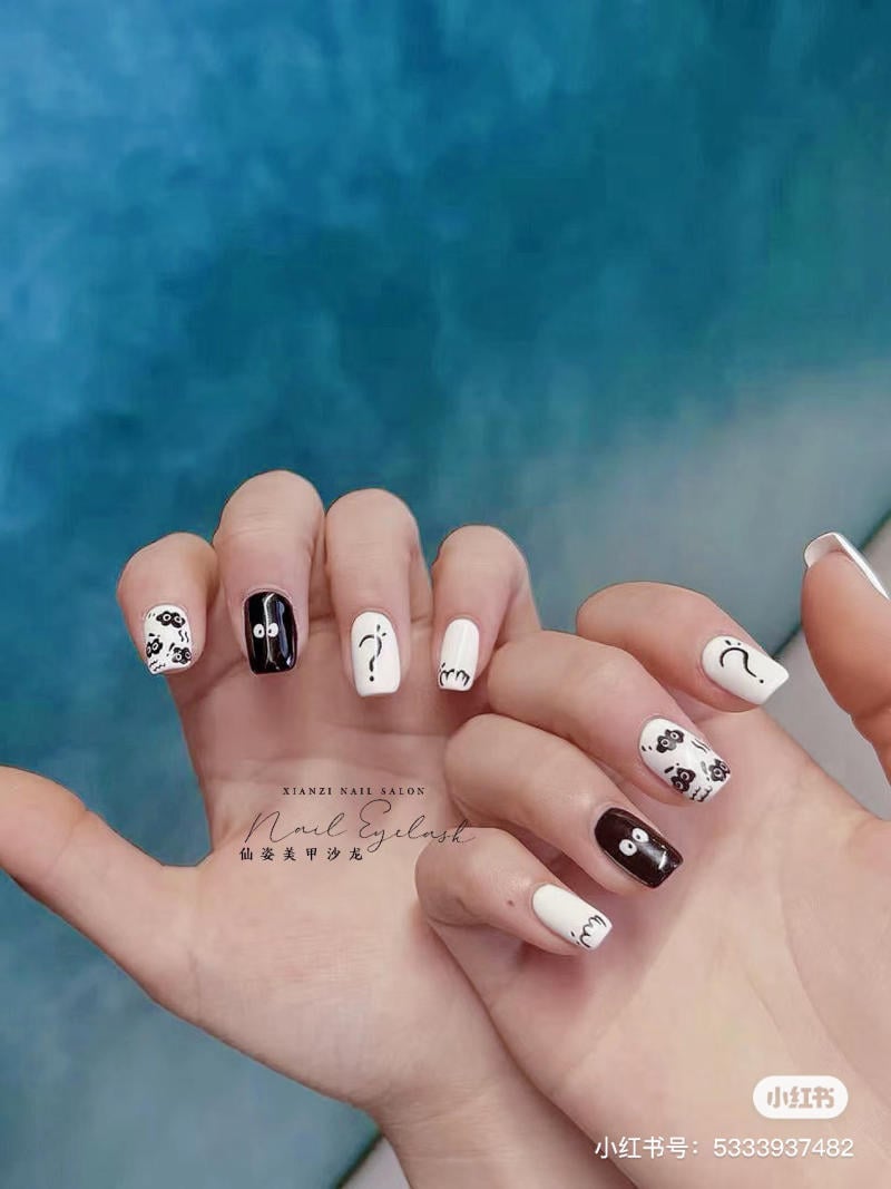 Bàn tay với móng tay được trang trí họa tiết đen trắng trên nền xanh.