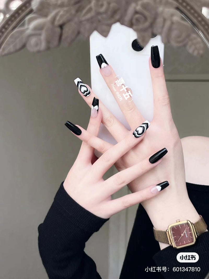 Tay đeo đồng hồ vàng, móng tay đen trắng họa tiết, cầm điện thoại trắng trước gương.