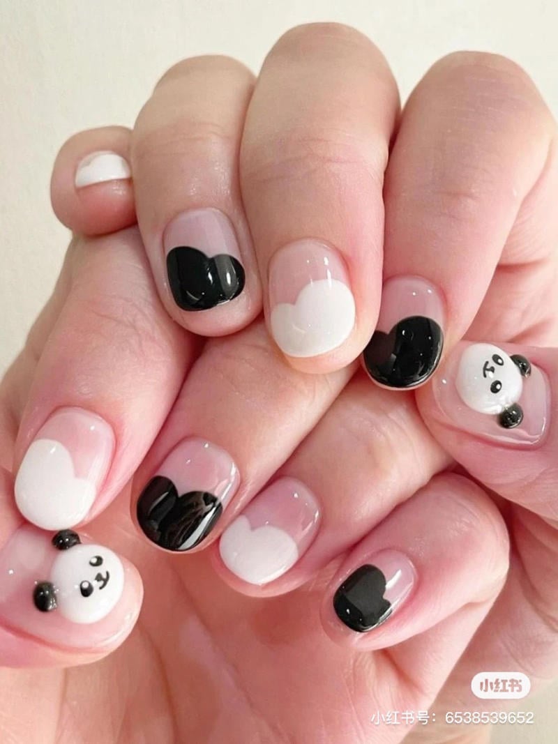nail-den-trang__8__91b54d74e4974a3e8afe7ef72071ec43 Móng tay được trang trí hình gấu trúc và họa tiết trái tim đen trắng, trên nền trong suốt.