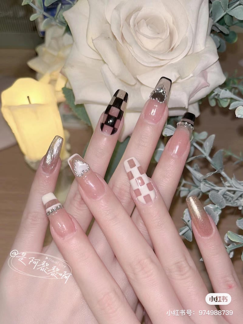 Bàn tay với móng tay dài, được trang trí họa tiết đa dạng, nền có hoa hồng trắng và nến vàng.
