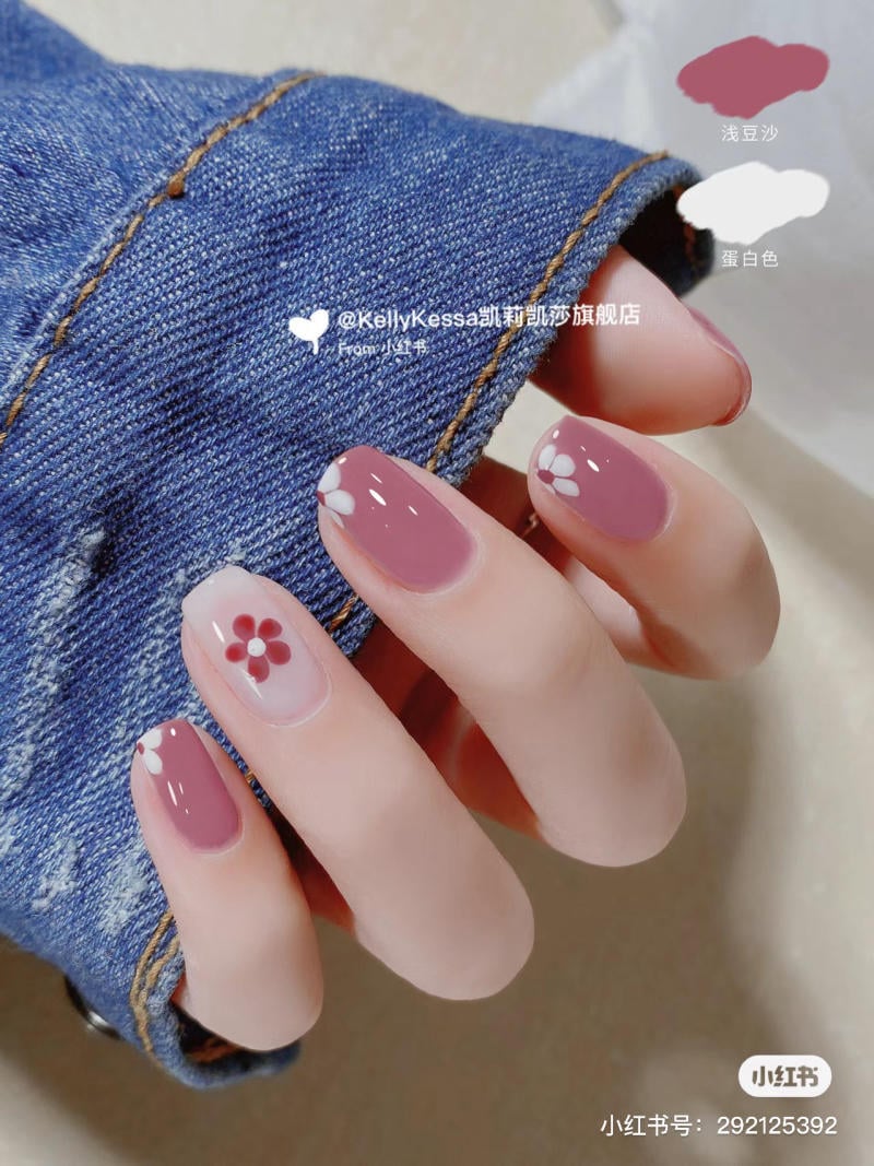 Tay với móng tay sơn màu hồng, có họa tiết hoa trắng, đặt trên nền vải denim xanh.