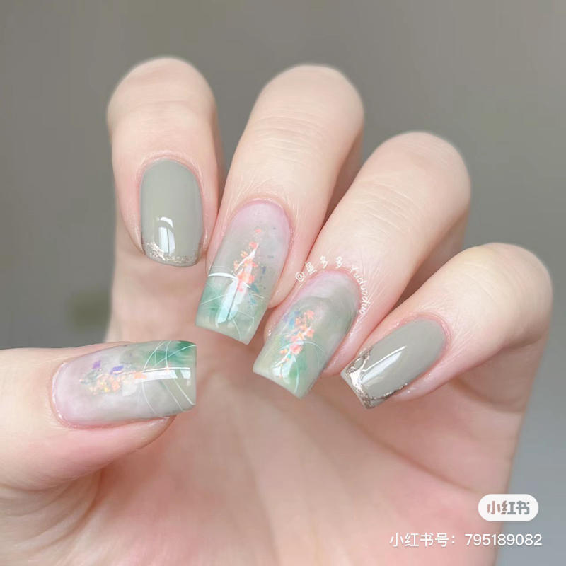 Bàn tay với móng tay được sơn màu xám và xanh lá, trang trí hình hoa và họa tiết tinh tế.