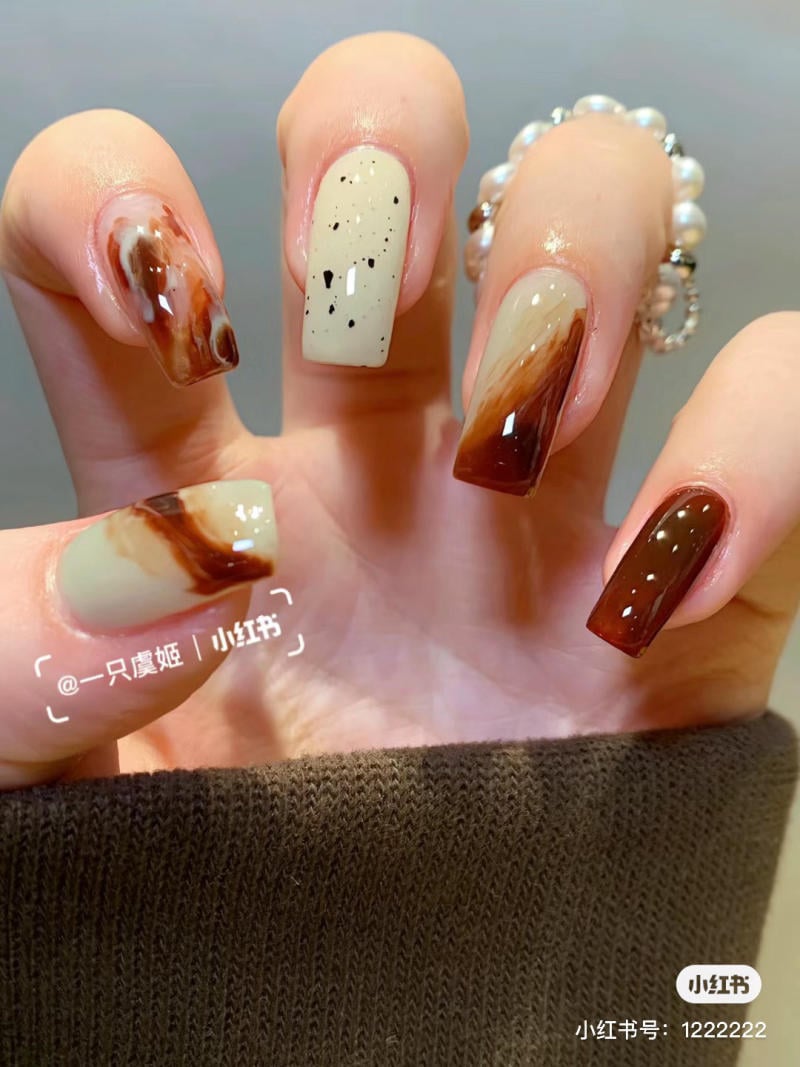 Bàn tay với móng tay được sơn nghệ thuật, màu nâu và kem, đan xen họa tiết vân và đốm đen.