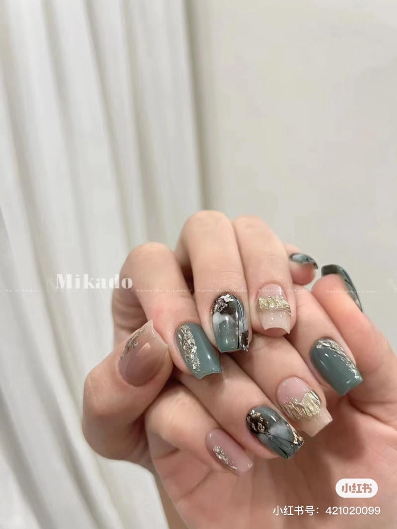 Bàn tay với móng tay được sơn màu xanh và nâu, có họa tiết trang trí ánh kim và hoa văn nghệ thuật.