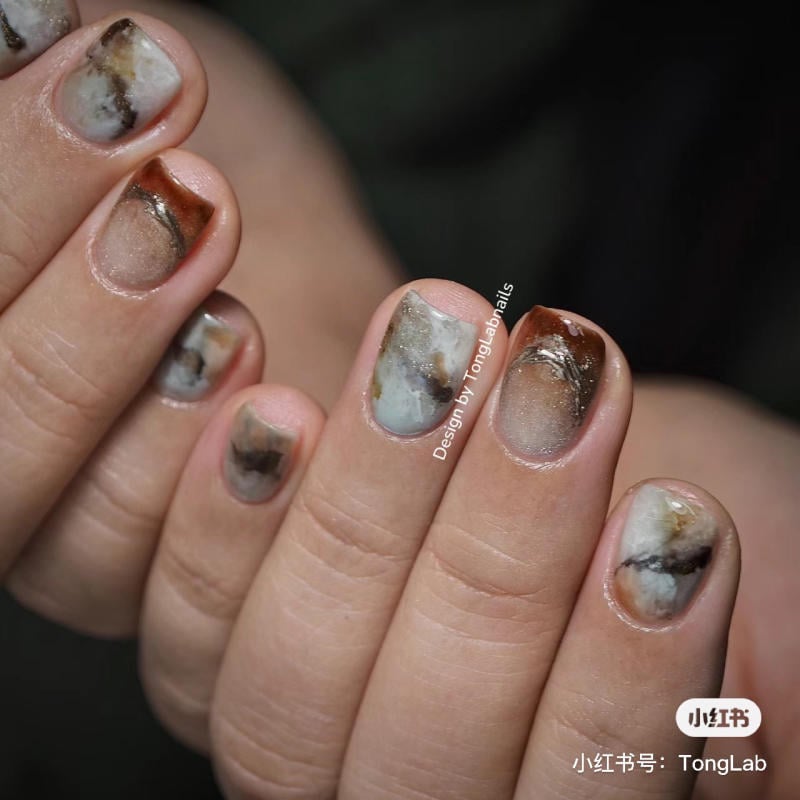 Bàn tay với móng tay được trang trí nghệ thuật, họa tiết vân đá màu nâu và trắng.