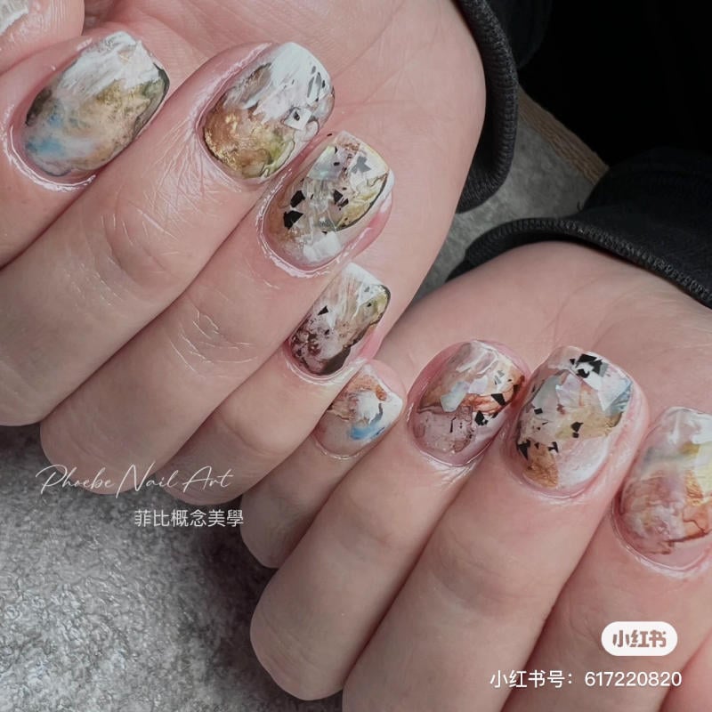 Bàn tay với móng tay được vẽ nghệ thuật, họa tiết trừu tượng nhiều màu sắc, nền bề mặt màu xám.