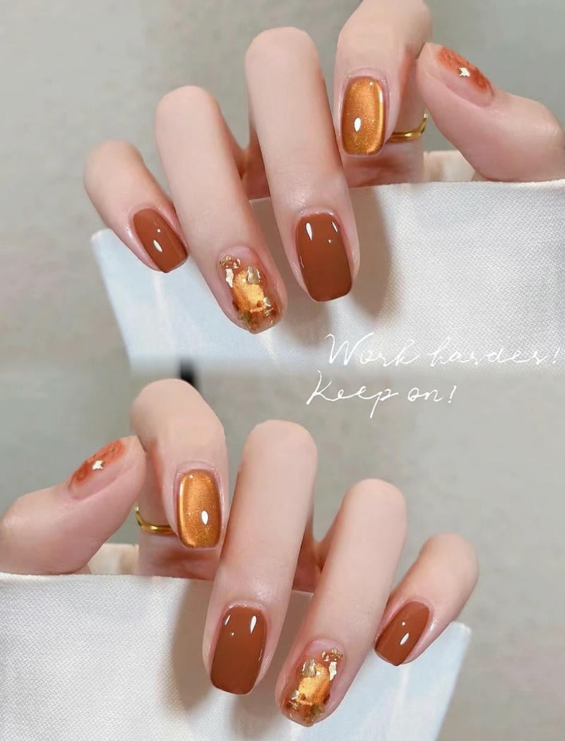 B&agrave;n tay với m&oacute;ng tay được sơn m&agrave;u n&acirc;u v&agrave; v&agrave;ng, c&oacute; họa tiết trang tr&iacute; v&agrave;ng &aacute;nh kim.