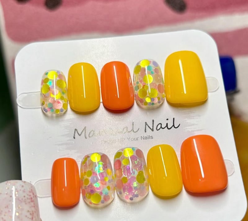 Bộ m&oacute;ng giả với c&aacute;c m&agrave;u sắc v&agrave;ng, cam, v&agrave; hoa văn chấm bi nhiều m&agrave;u tr&ecirc;n nền bảng trưng b&agrave;y.