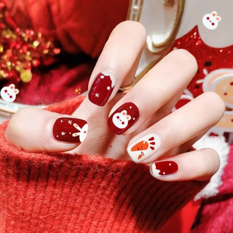 Bàn tay với móng tay được sơn màu đỏ và trắng, trang trí họa tiết thỏ và cà rốt, mặc áo len đỏ.