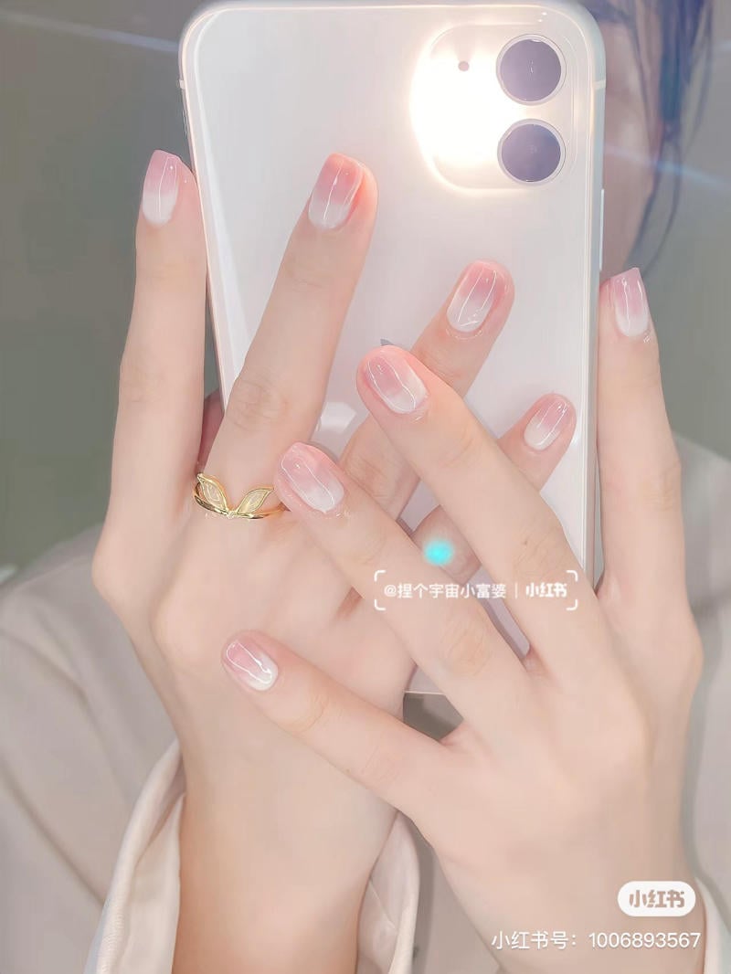 Tay cầm điện thoại, móng tay sơn màu hồng nhạt, đeo nhẫn vàng hình lá.