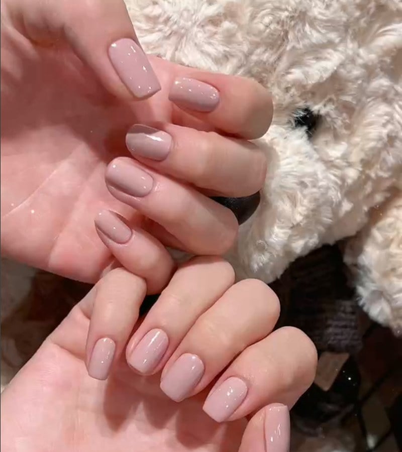 Bàn tay với móng tay sơn màu hồng nhạt, nền là vải lông mềm mại màu trắng.