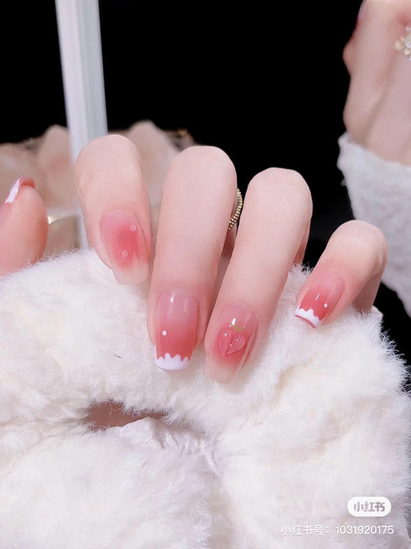 Bàn tay với móng tay sơn màu hồng nhạt, họa tiết trắng và hình trái tim nhỏ.