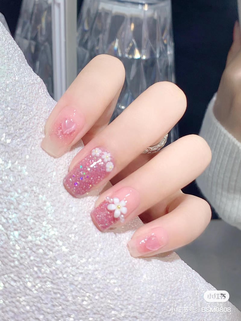 Bàn tay với móng tay trang trí hoa và kim tuyến lấp lánh, nền vải ánh kim.