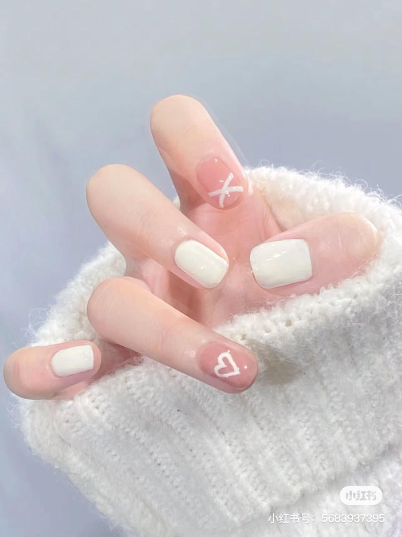 Tay đeo áo len trắng, móng tay sơn màu trắng và hồng, có họa tiết tim và chữ X trắng.