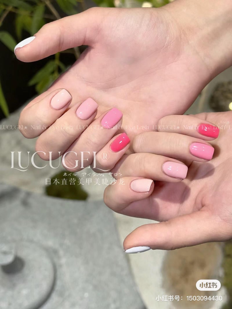 Hai bàn tay với móng được sơn màu hồng nhạt và đậm, nền là cây cối mờ.