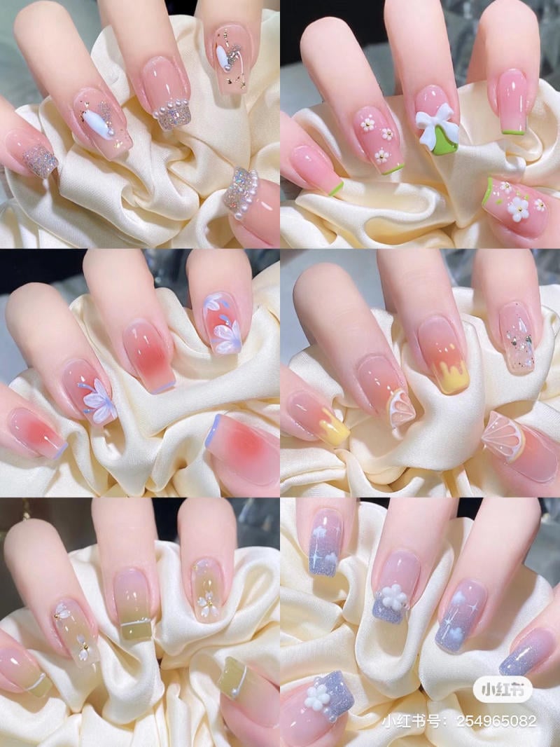 Bộ móng tay được trang trí với nhiều họa tiết hoa và màu sắc khác nhau, đặt trên nền vải satin trắng.