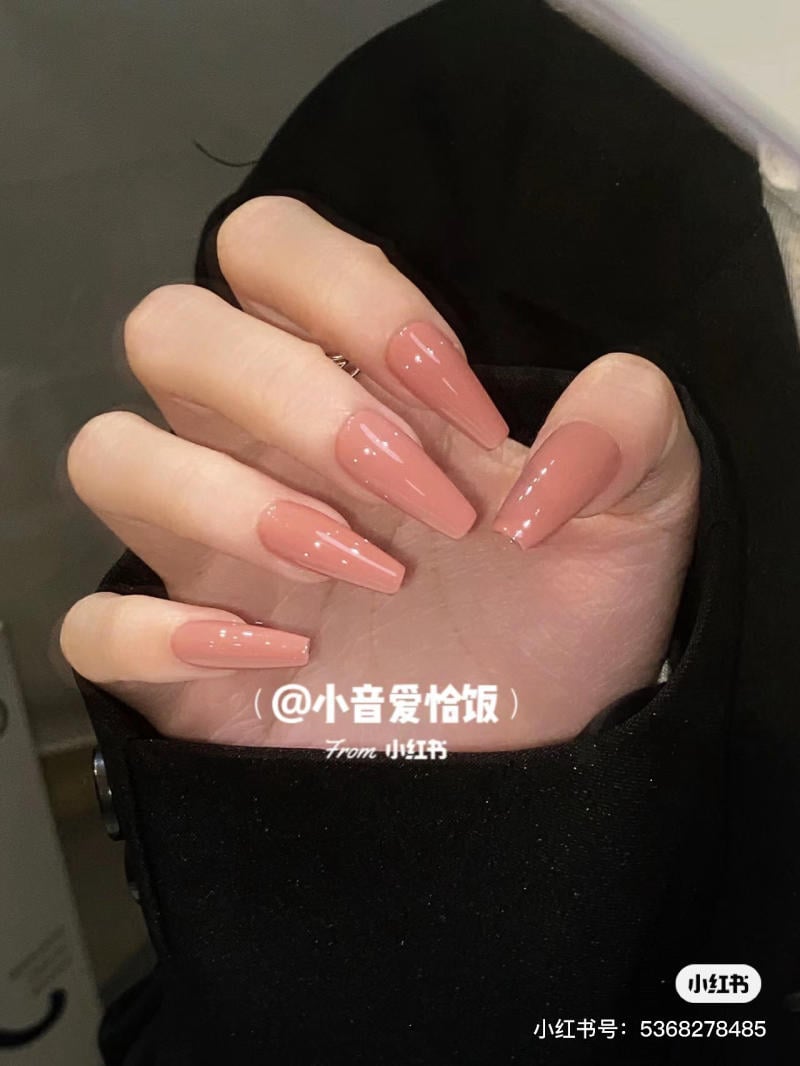 Bàn tay với móng dài, sơn màu hồng nude, ánh bóng, trên nền áo tối màu.