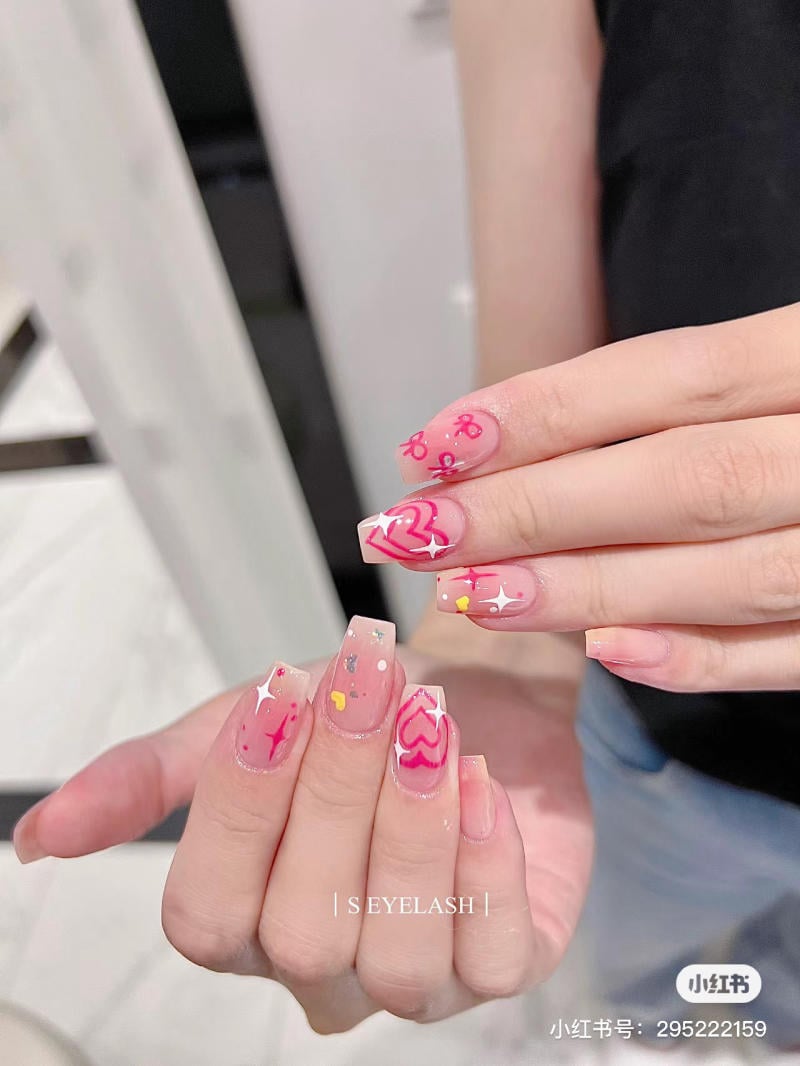 Bàn tay với móng tay sơn màu hồng, trang trí họa tiết trái tim và hoa văn nghệ thuật.